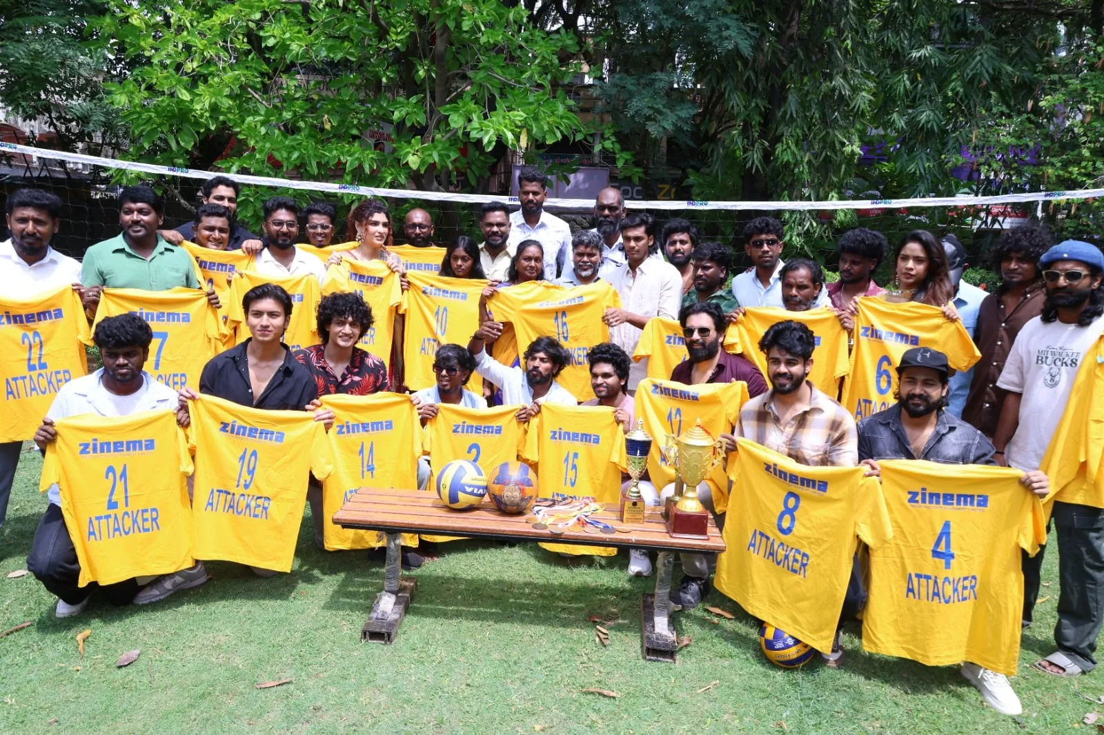 The Attakkar cast holding numbered volleyball jerseys beside a net at the film's launch