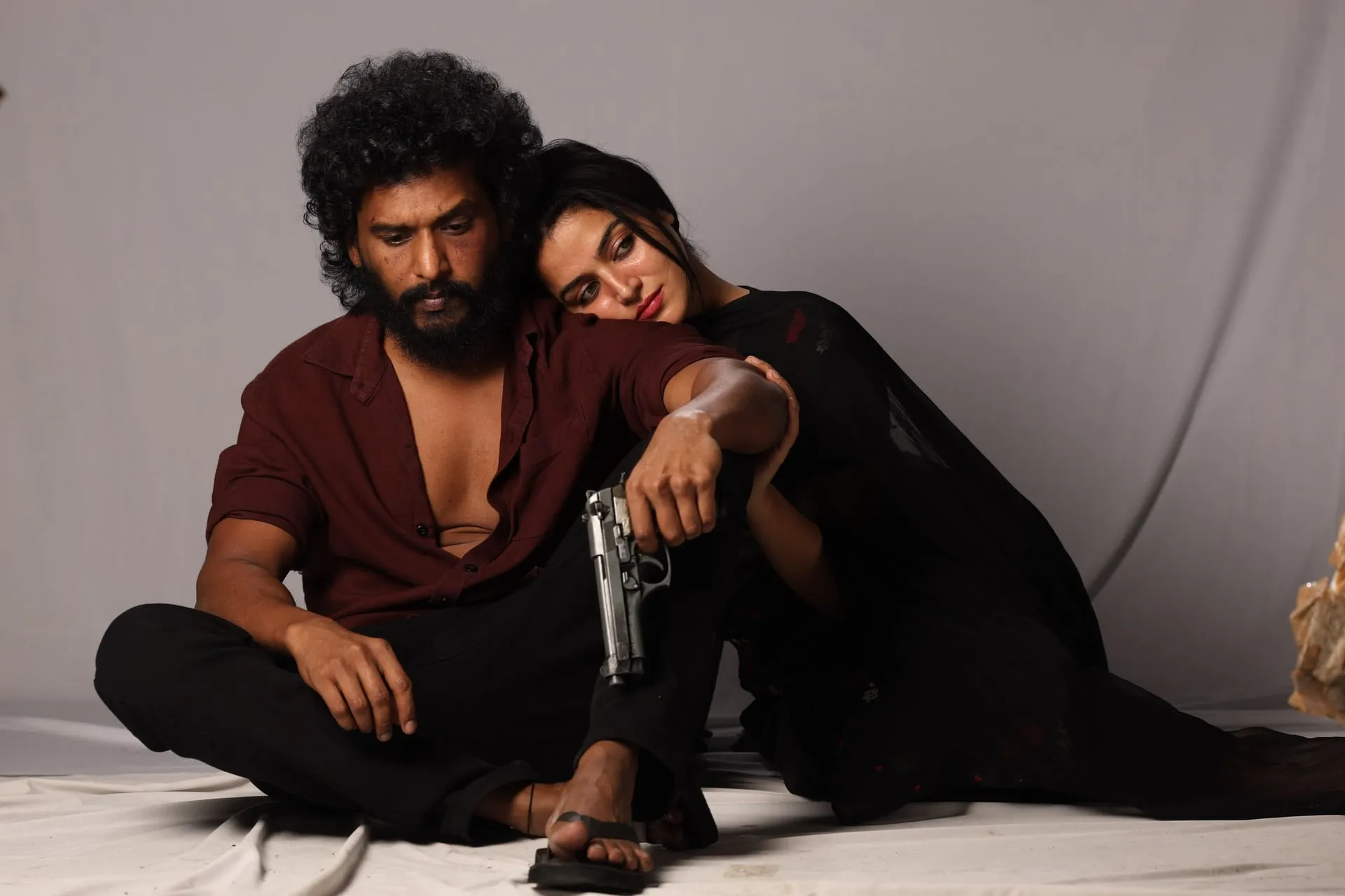 Lokesh Kanagaraj as Devadas sits with a pistol in hand while Wamiqa Gabbi's Chandra leans on his shoulder against a plain studio backdrop