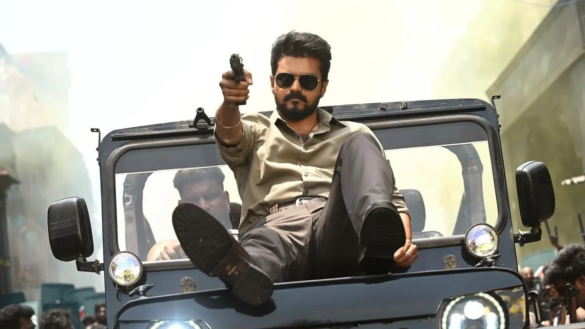 Vijay perched on a jeep bonnet aiming a pistol, in sunglasses and an olive shirt, in a still from Jana Nayagan