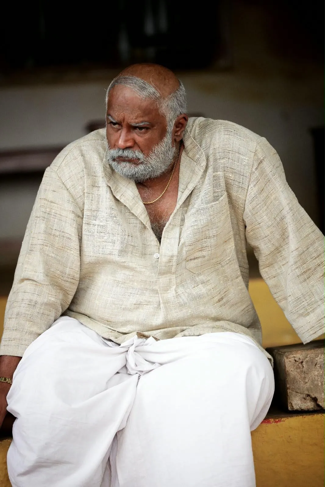 Vettai Muthukumar with a white beard, seated in a cream kurta and veshti