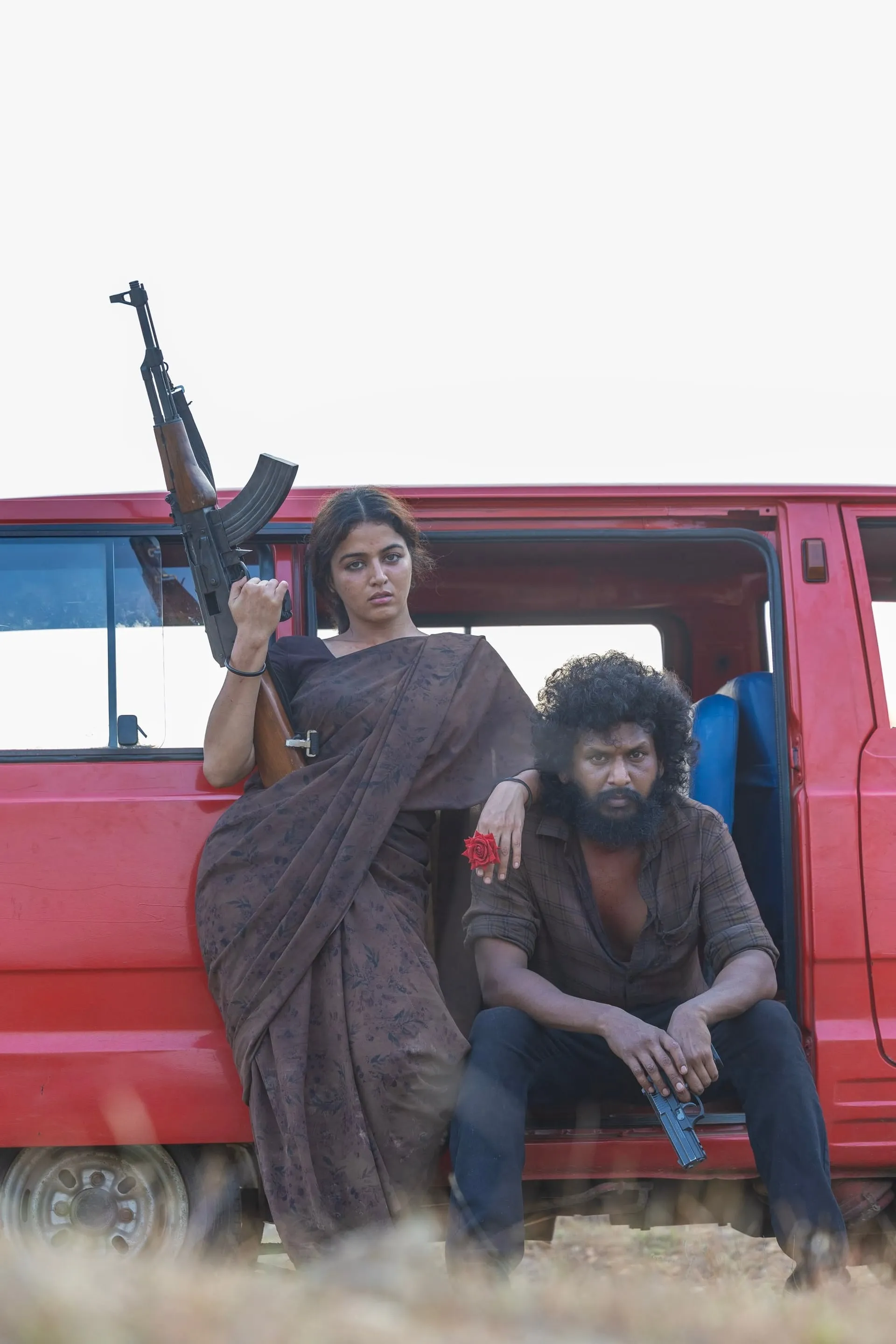 Wamiqa Gabbi holds an AK-47 beside a red van while Lokesh Kanagaraj sits in its doorway with a pistol