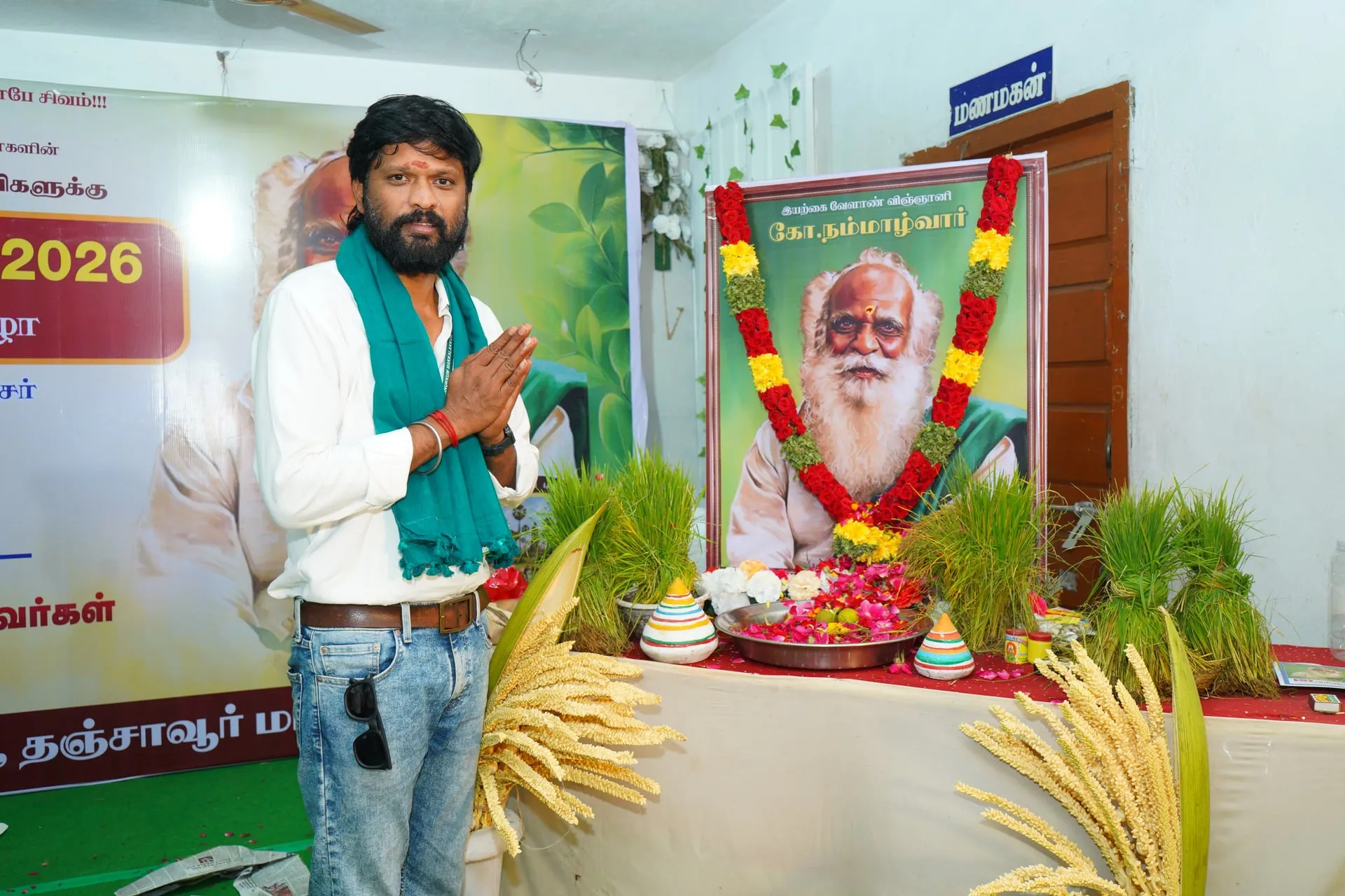 Soundararaja paying his respects at a portrait of Nammalvar, with paddy saplings and millets laid out