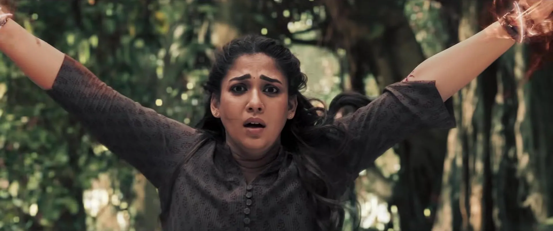 Nayanthara with her arms flung out in a forest, looking terrified