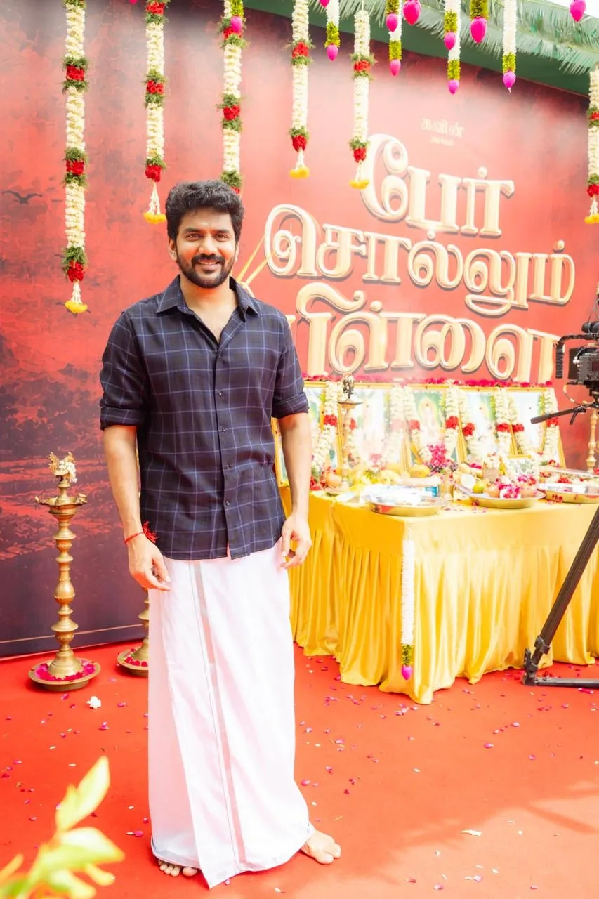 Kavin at the Per Sollum Pillai pooja, in a checked shirt and veshti in front of the film's title backdrop.
